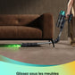 Personne utilisant un aspirateur balai équipé d'un tube et d'une tête de brosse éclairée par une LED verte vive, pour nettoyer sous un canapé en velours brun. Le slogan "Glissez sous les meubles sans vous baisser" apparaît en bas de l'image.